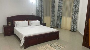 Een slaapkamer met een houten bed, witte beddengoed, een nachtkastje en vloerkleden met een patroon.