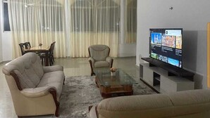 Een woonkamer met een bank, fauteuil en salontafel. Een televisie staat op een dressoir aan de rechterkant.