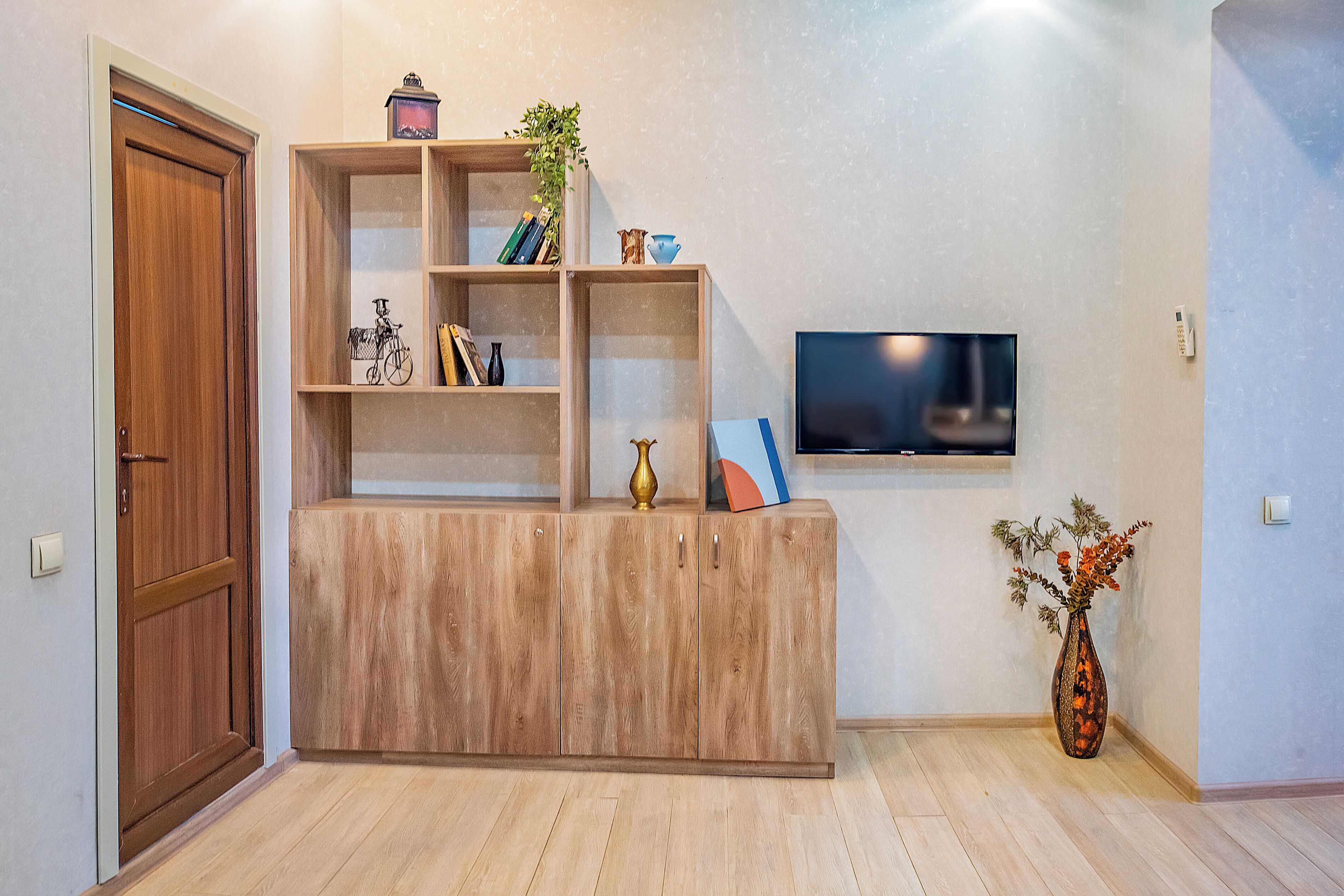 A wooden cabinet with shelves, a television mounted on the wall, and a vase with flowers.