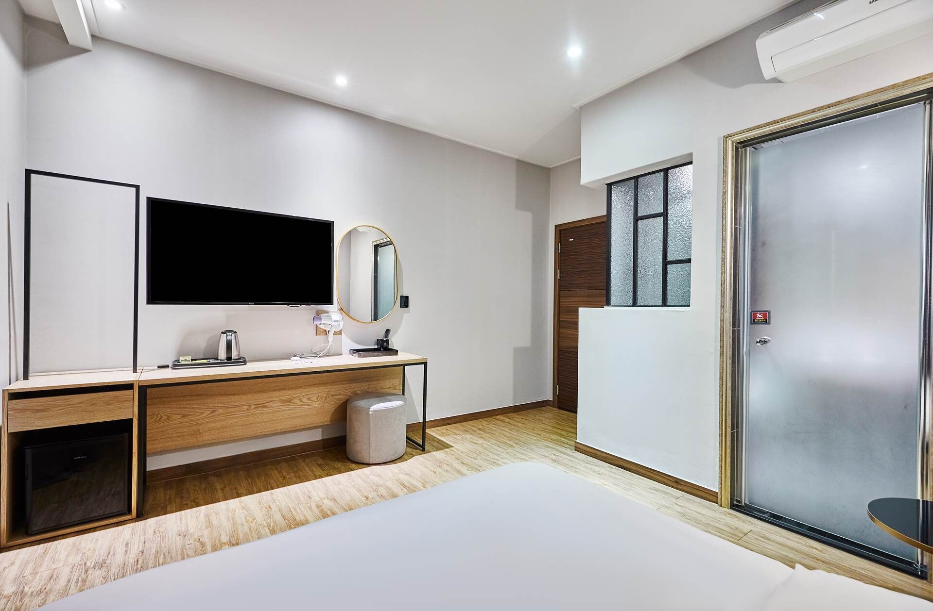A modern hotel room with a large bed, a flat-screen TV, a wooden vanity, a mirror, and a sliding door with frosted glass.