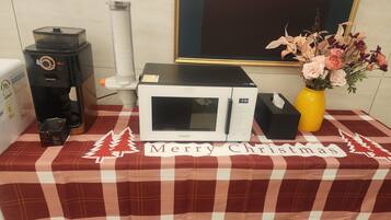 A microwave on a checkered tablecloth with a 'Merry Christmas' message, a coffee maker, a vase with flowers, and a framed artwork on the wall.