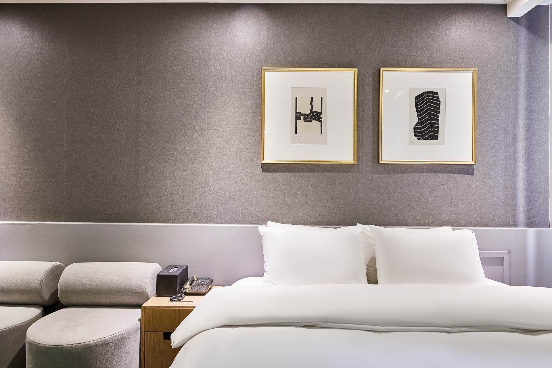 A hotel room with a bed, two bedside tables, and two framed artworks on the wall.