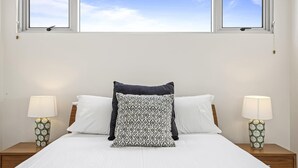 Uma cama bem arrumada com lençóis brancos, duas luminárias de cabeceira e um travesseiro estampado.