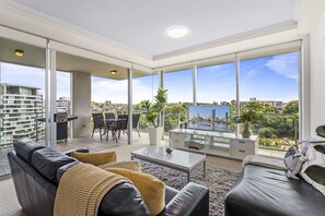A spacious living room with a large TV, comfortable seating, and a balcony with a city view. - High-Floor 2-Bed CBD Unit With Views & Amenities (Brisbane City)
