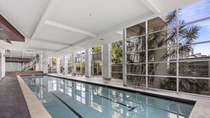 Uma piscina com paredes de vidro transparente, chão de azulejos e escada que leva a um andar superior.