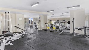 Uma academia com diversos equipamentos de exercício, incluindo esteiras e aparelhos elípticos, dispostos em um espaço amplo e bem iluminado.