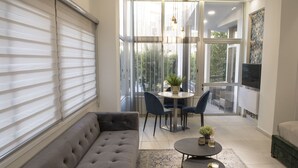 A modern living room with a grey sofa, a round coffee table, and a dining area with chairs and a small table. - STAY Glam Skin Studio (Nicosia)