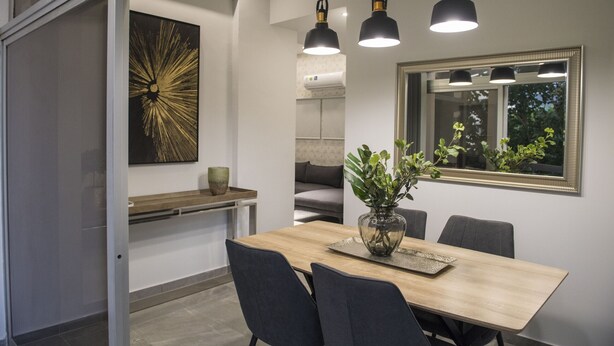 A modern dining area with a wooden table, dark chairs, and pendant lighting. - STAY Urban Skin Suite (Nicosia)