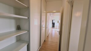 A narrow hallway with white walls and wooden flooring leading to a room with a kitchen area. - STAY Mystique City Penthouse (Limassol)