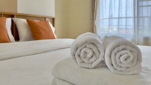 A neatly made bed with two rolled white towels and a few pillows in a hotel room. - Sriracha Avenue (Si Racha)