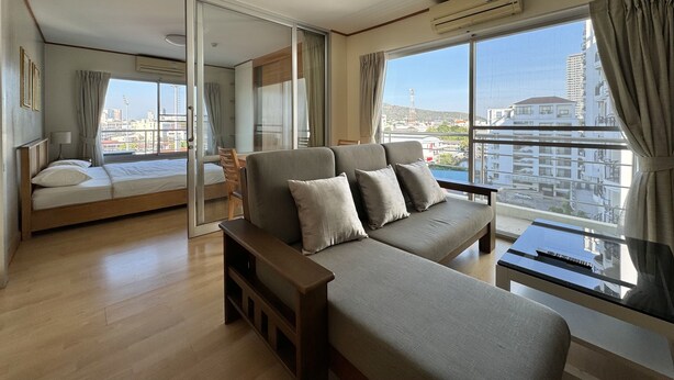 A modern hotel room with a large bed, a sofa, a small table, and a balcony with a city view. - Sriracha Avenue (Si Racha)
