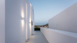 Un couloir étroit aux murs blancs, d’où l’on aperçoit une ville et une colline au loin.