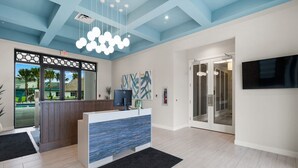 A modern reception area with a wooden reception desk, a large digital screen, and a blue and white patterned rug. - Adorable Townhouse 4Bed/3Bath/Pool/5Min Disney (Kissimmee)