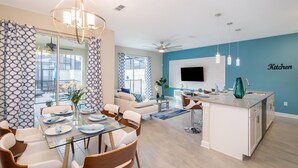 A modern kitchen with a built-in island, a dining area with a glass table, and a living room with a sofa and a TV. - Adorable Townhouse 4Bed/3Bath/Pool/5Min Disney (Kissimmee)