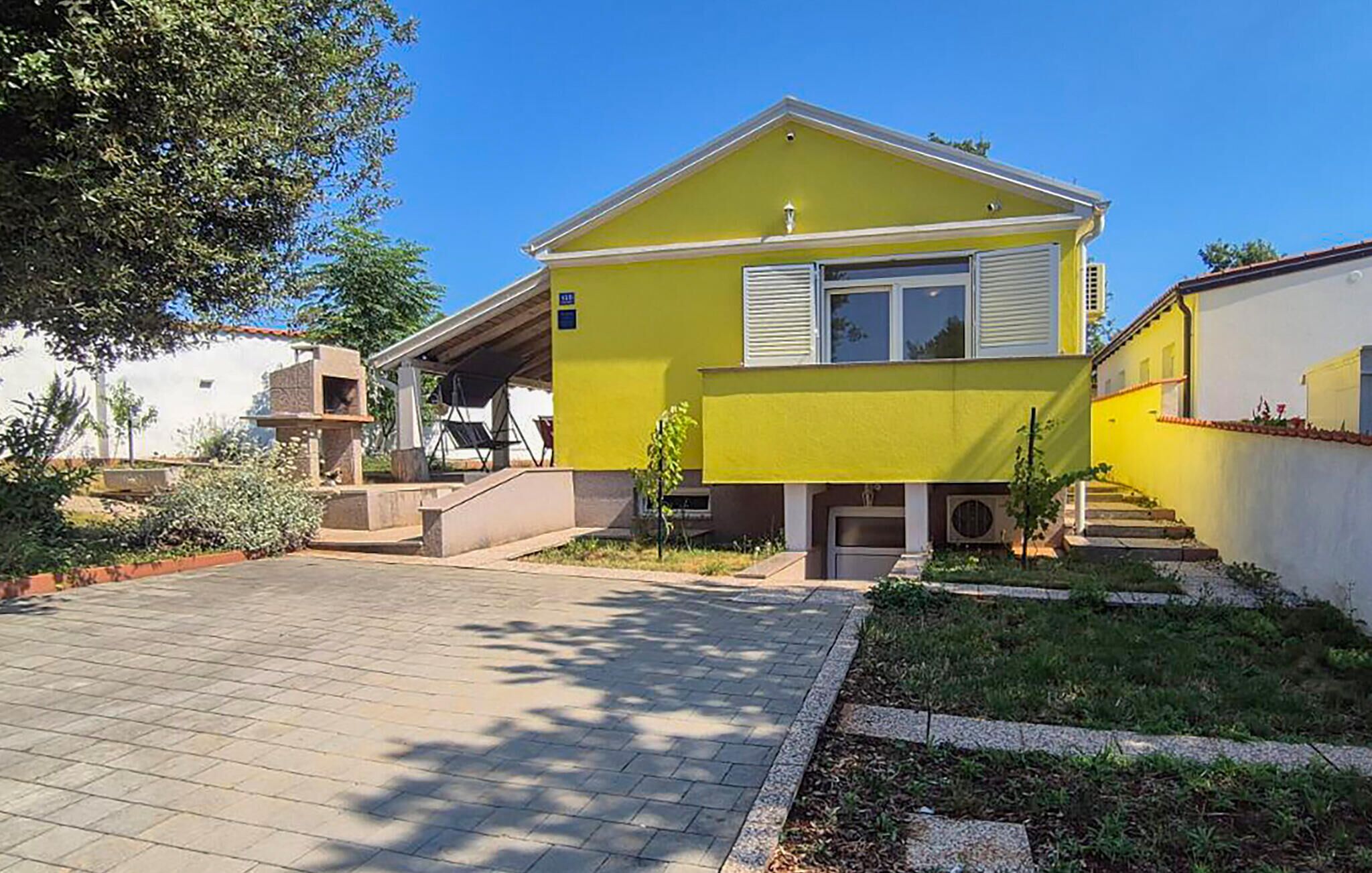Una casa amarilla con entrada pavimentada y un pequeño jardín.