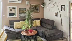 Ein Wohnzimmer mit einem grauen Ecksofa, einem runden Couchtisch aus Holz und zwei Blumentöpfen.