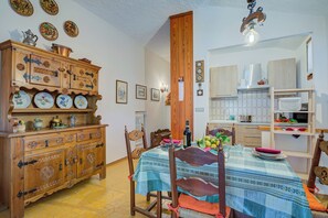 A dining area with a wooden cabinet, a table with a blue tablecloth, chairs, and a kitchen area in the background. - The Secret Garden in the City Center (Bardonecchia)