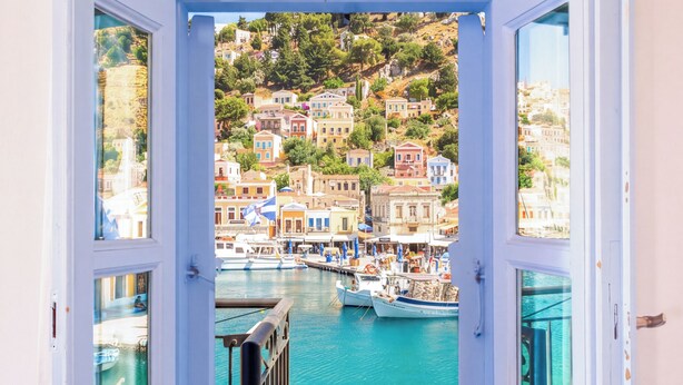 An open door leading to a balcony with a view of a harbor and colorful buildings. - Seafront - Harbour view Nikolakis (Symi)