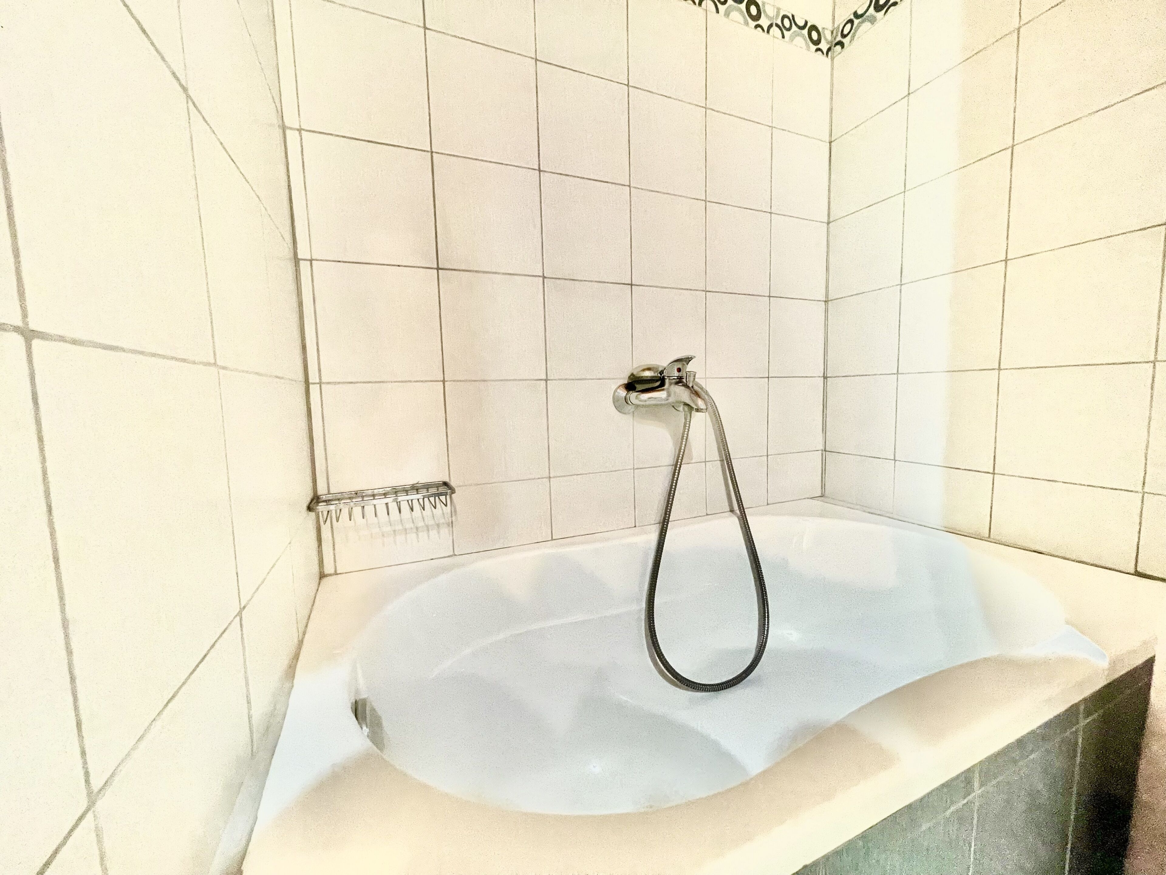 A bathroom with a bathtub, a shower head, and tiled walls.