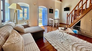 A spacious living room with a wooden staircase, a dining area with white chairs, and a large window with blue shutters. - Seafront - Harbour view Nikolakis (Symi)