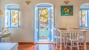 A room with a view of a harbor, a dining area with white chairs, and a painting of fruit on the wall. - Seafront - Harbour view Nikolakis (Symi)