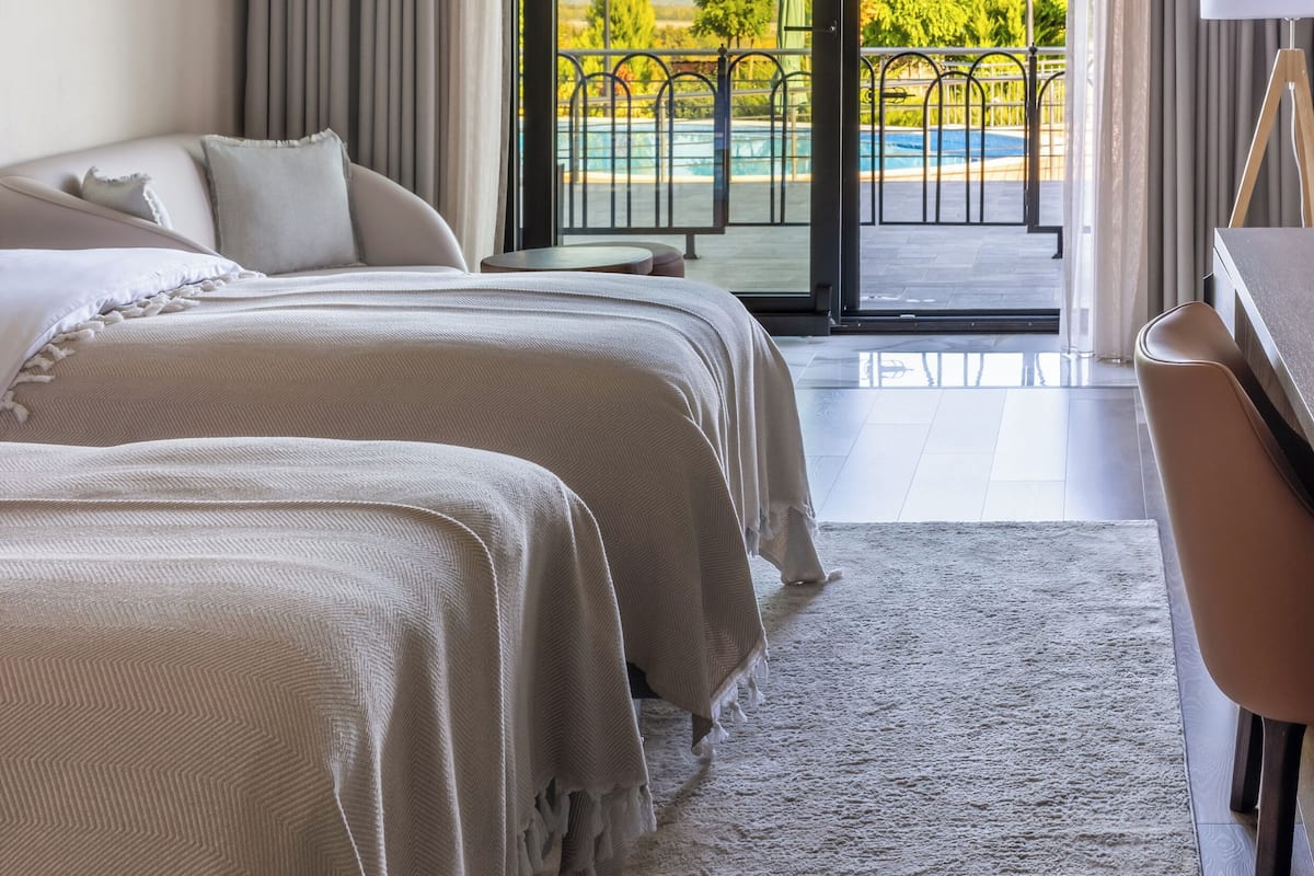 Une chambre d’hôtel avec deux lits, un bureau et une grande fenêtre donnant sur une piscine et un espace verdoyant.