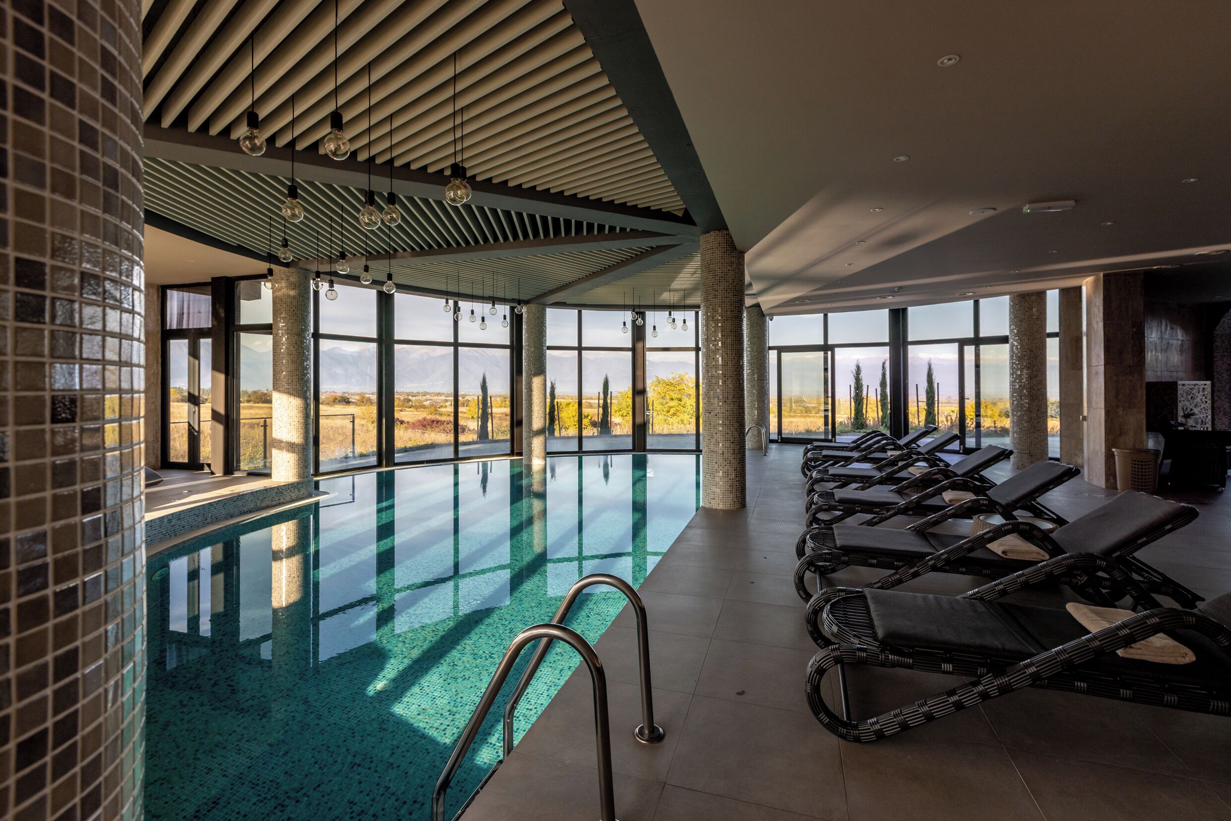 Piscina interior con vistas despejadas a montañas, sillas de descanso y techo de azulejos.