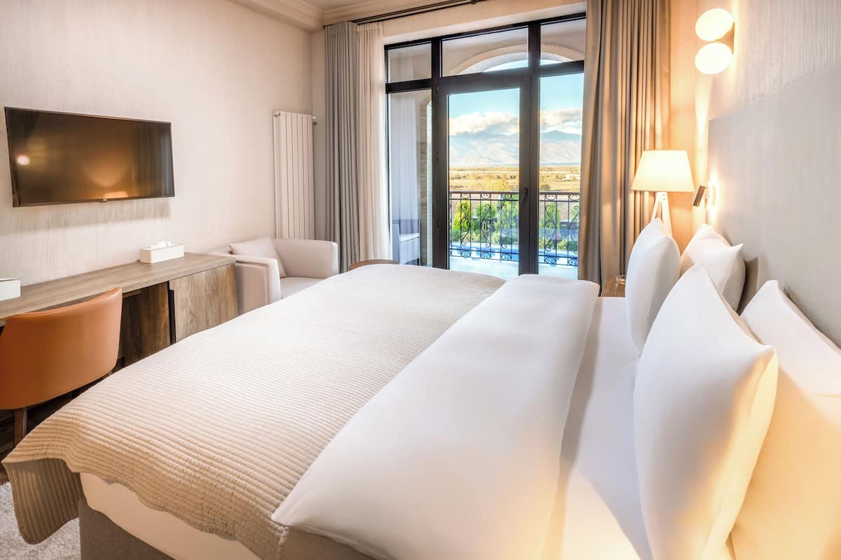 Une chambre d’hôtel dotée d’un grand lit, d’un bureau avec une chaise, d’un téléviseur fixé au mur et d’un balcon offrant une vue sur les montagnes.