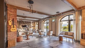A spacious living room with a fireplace, large windows, and a modern kitchen in the background. - Panorama Kakheti Resort (Gurjaani)