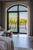 Habitación de hotel moderna con un amplio ventanal corredero que da a una zona de piscina exterior, un sofá, una pequeña mesa redonda y un banco.