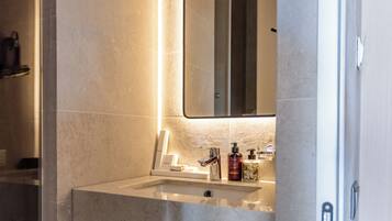A modern bathroom with a marble sink, a mirror, and a green storage box.