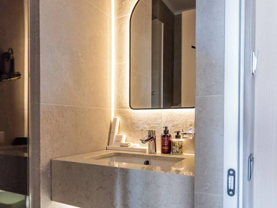 A modern bathroom with a marble sink, a mirror, and a green storage box.