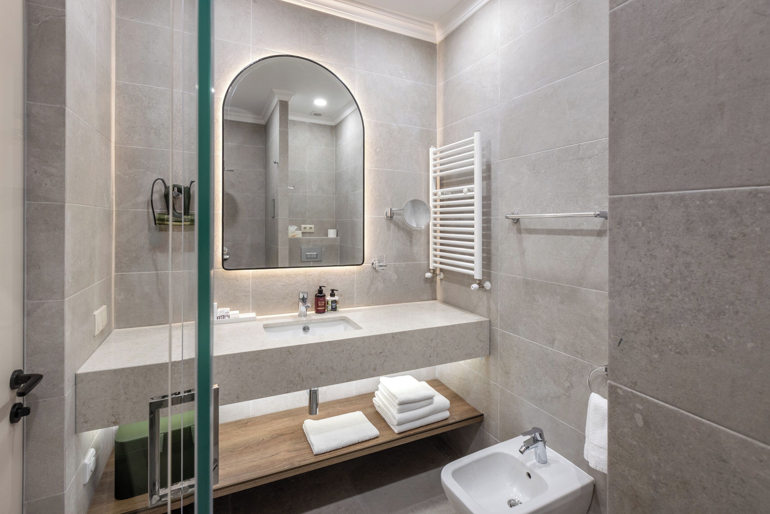 A modern bathroom with a glass shower enclosure, a wooden vanity, a white sink, and a mirror with an under-cabinet light.