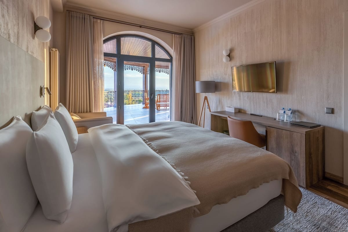 Une chambre d’hôtel avec un grand lit, un bureau, une télévision et un balcon avec vue.
