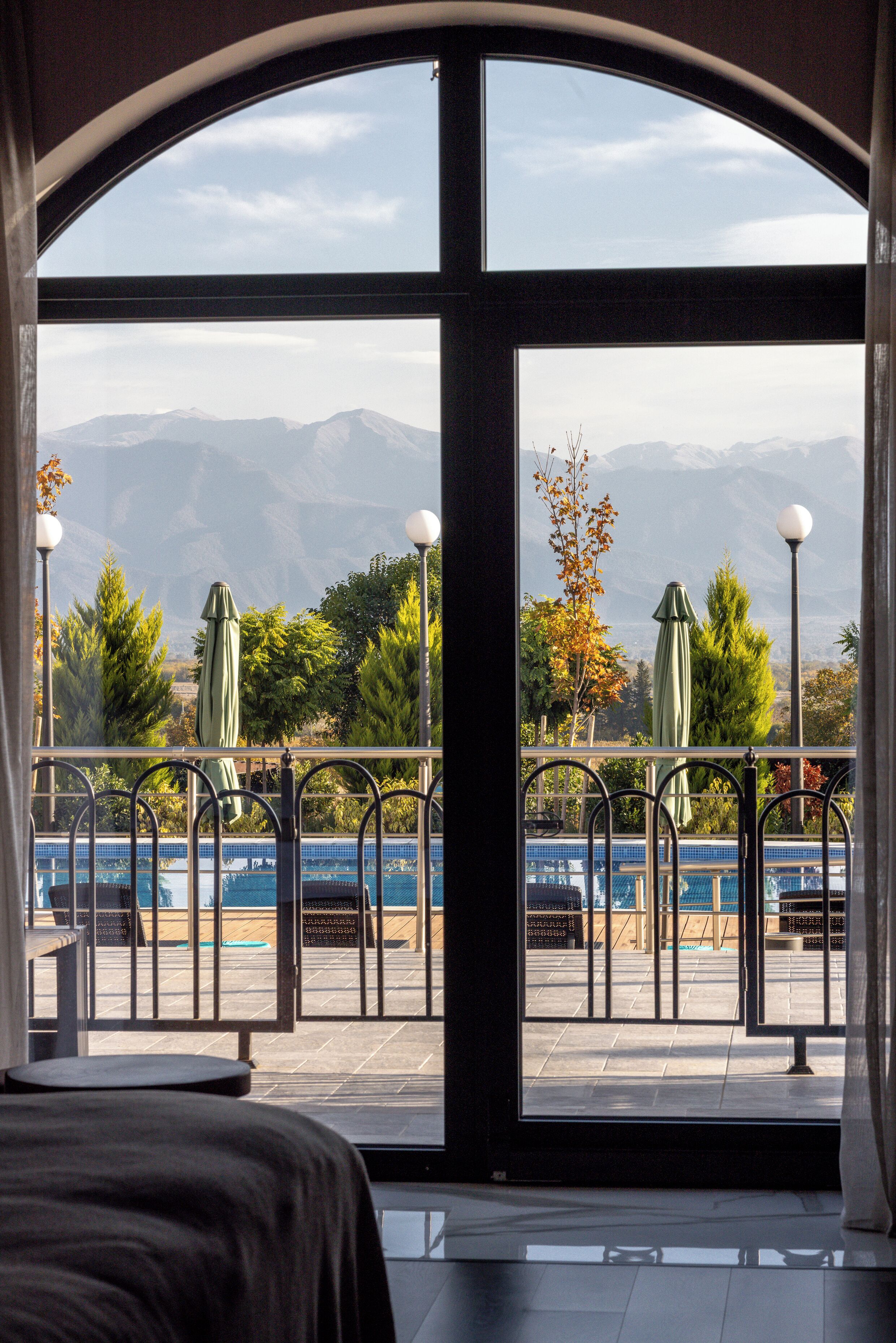 Habitación con un amplio ventanal que ofrece vistas a montañas y un área de piscina con sombrillas.