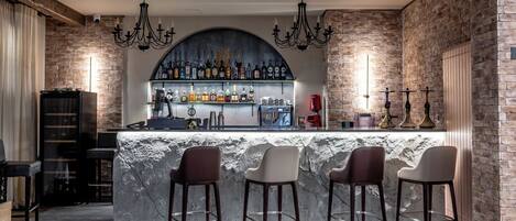 A bar area with a stone counter, bar stools, and a variety of bottles.
