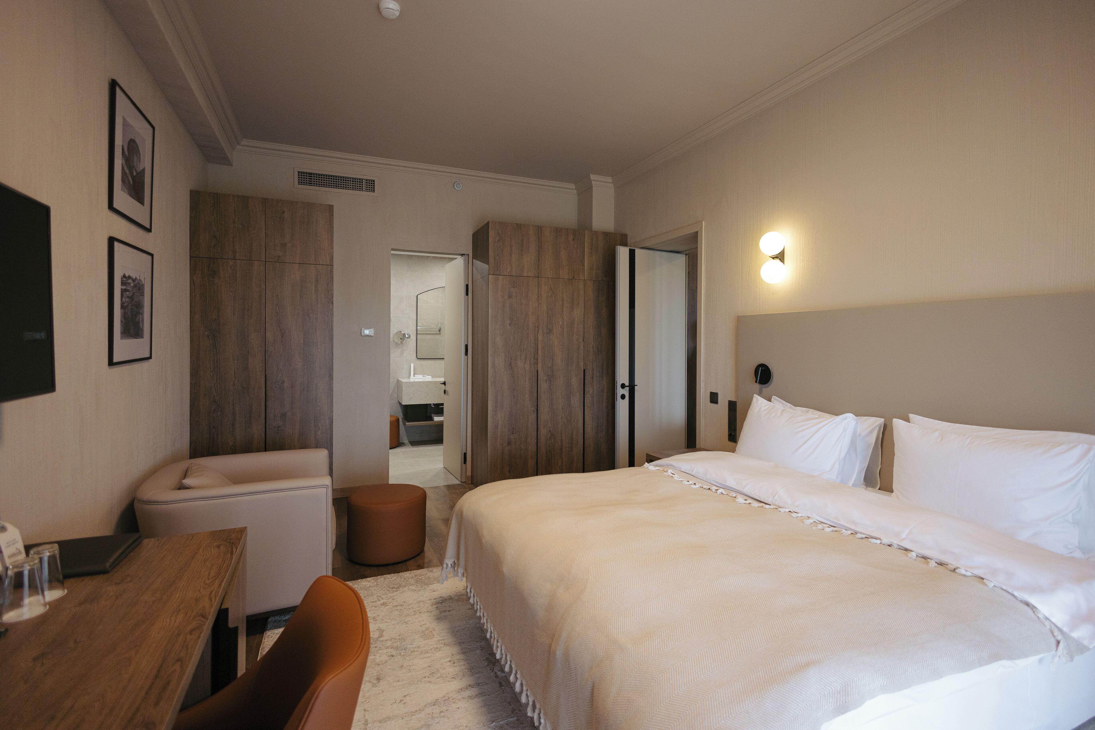 Una habitación de hotel con una cama grande, un escritorio, una silla, un taburete pequeño y un armario.