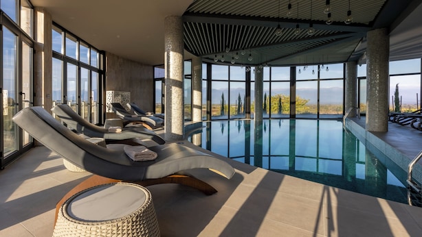 A modern indoor pool area with lounge chairs and a view of the landscape. - Panorama Kakheti Resort (Gurjaani)