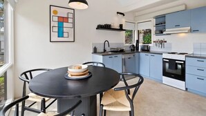 A modern kitchen with light blue cabinets, a black dining table with chairs, and a pendant light. - Boxy's Beach House: Perfect Location - Sea ViewsPeace & Quiet - Walk Anywhere (Lorne)
