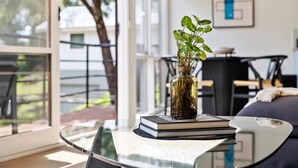 A modern living room with a glass coffee table, a vase with green plants, and a stack of books. - Boxy's Beach House: Perfect Location - Sea ViewsPeace & Quiet - Walk Anywhere (Lorne)