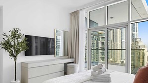 A modern hotel room with a large bed, a flat-screen TV, a potted plant, and a view of high-rise buildings. - Silkhaus Trident Oceanic - Dubai Marina (Dubai)
