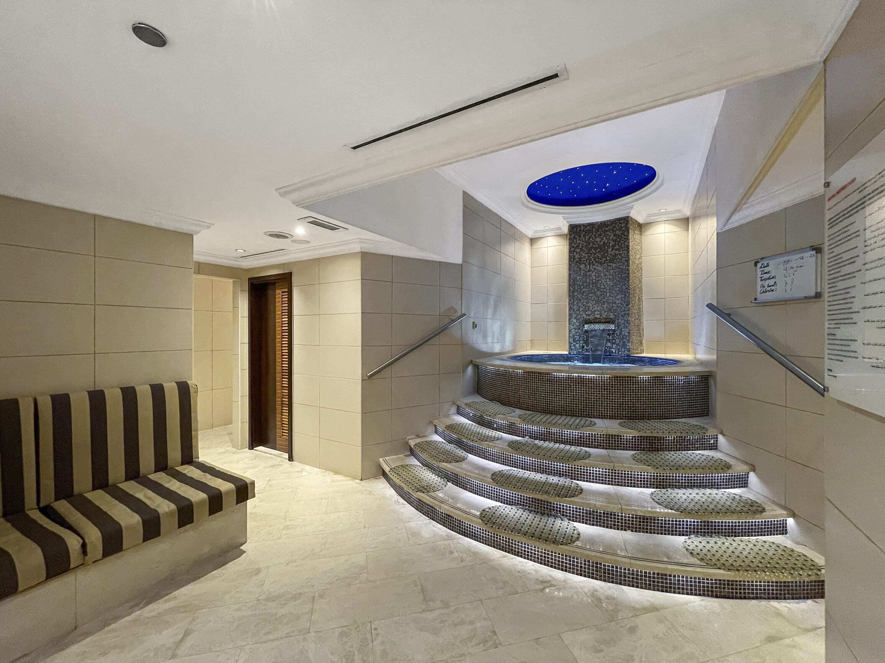 A modern interior with a curved staircase leading to a hot tub area, a seating area with striped cushions, and a wall-mounted information board.