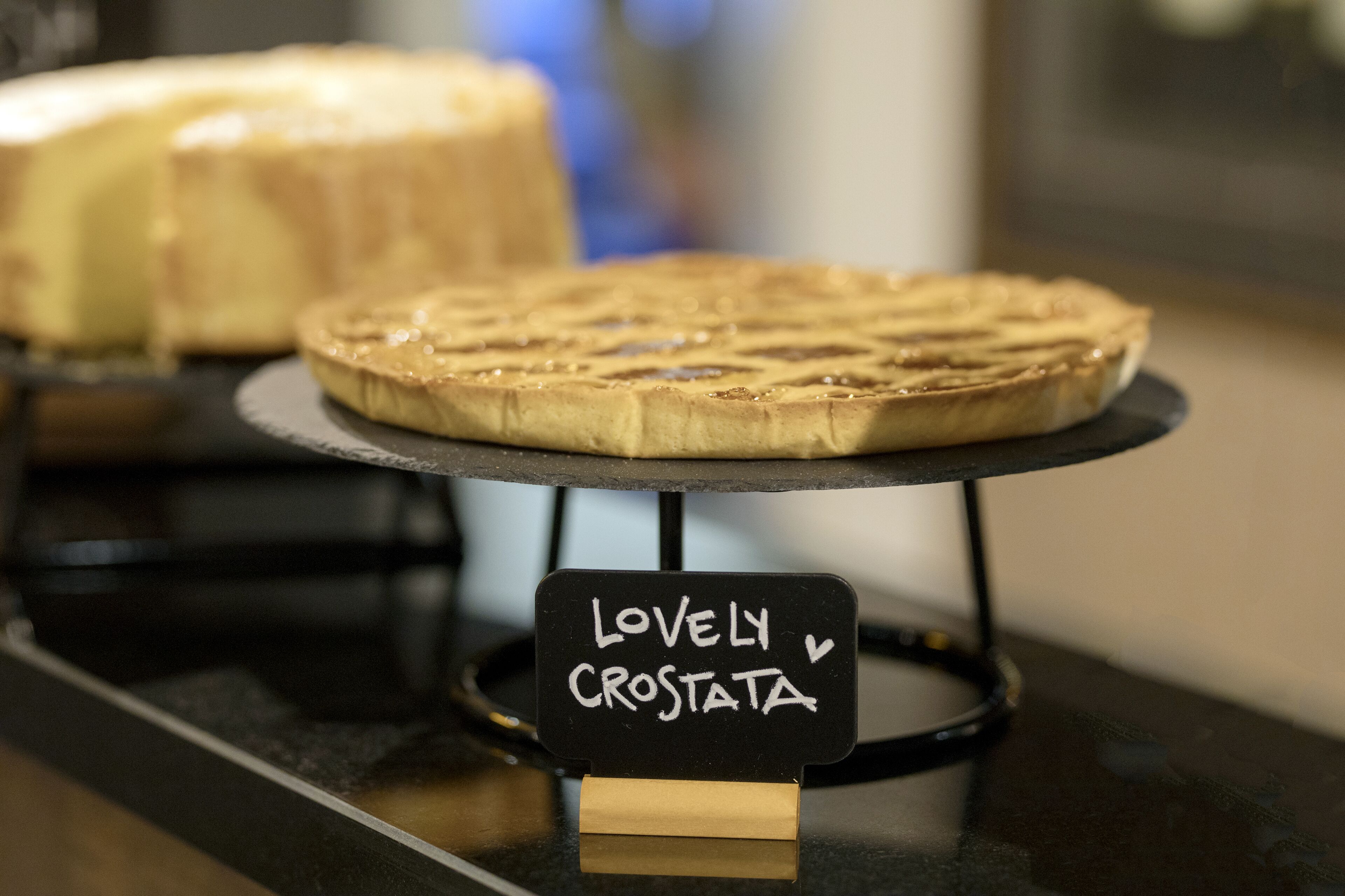 A dessert display with a sign reading "Lovely Crostata" on a black stand.