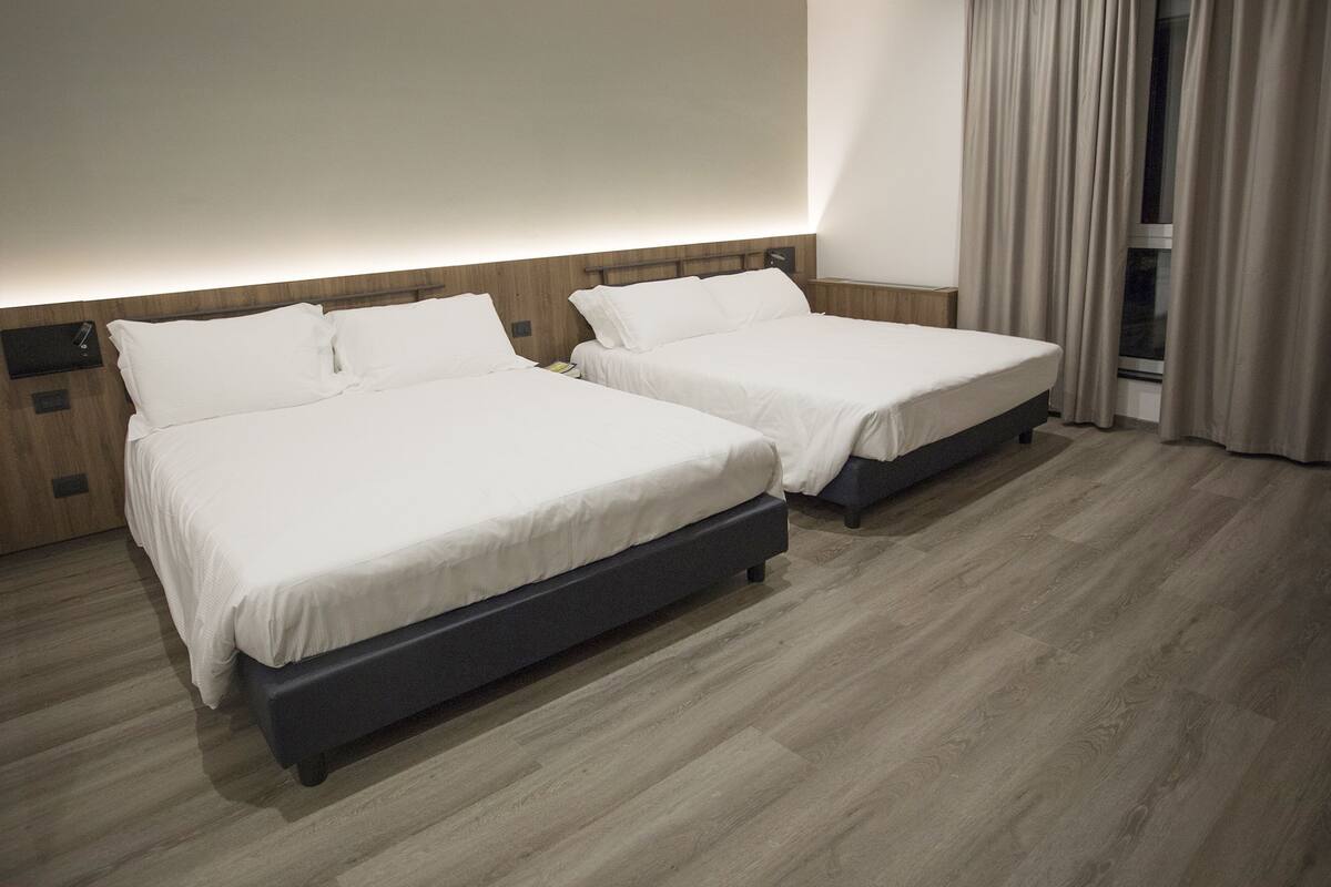 Two single beds with wooden headboards, a wooden floor, and a window with curtains.