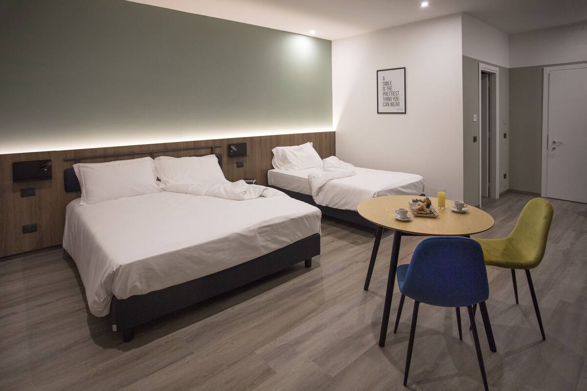 A hotel room with two beds, a small round table with chairs, and a wall-mounted light fixture.