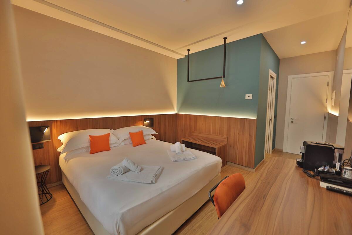 A hotel room with a bed, a desk, a chair, a wardrobe, and a door.