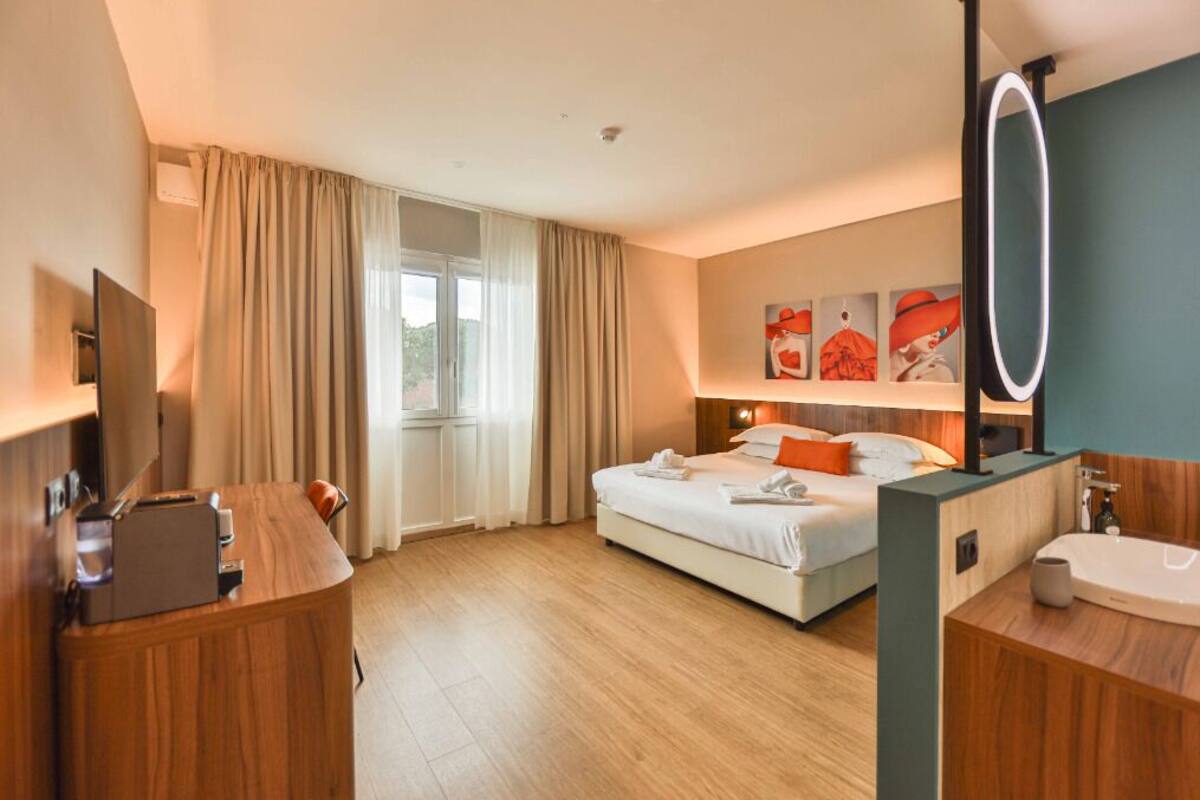 A hotel room with a bed, a desk, a mirror, and a bathroom.