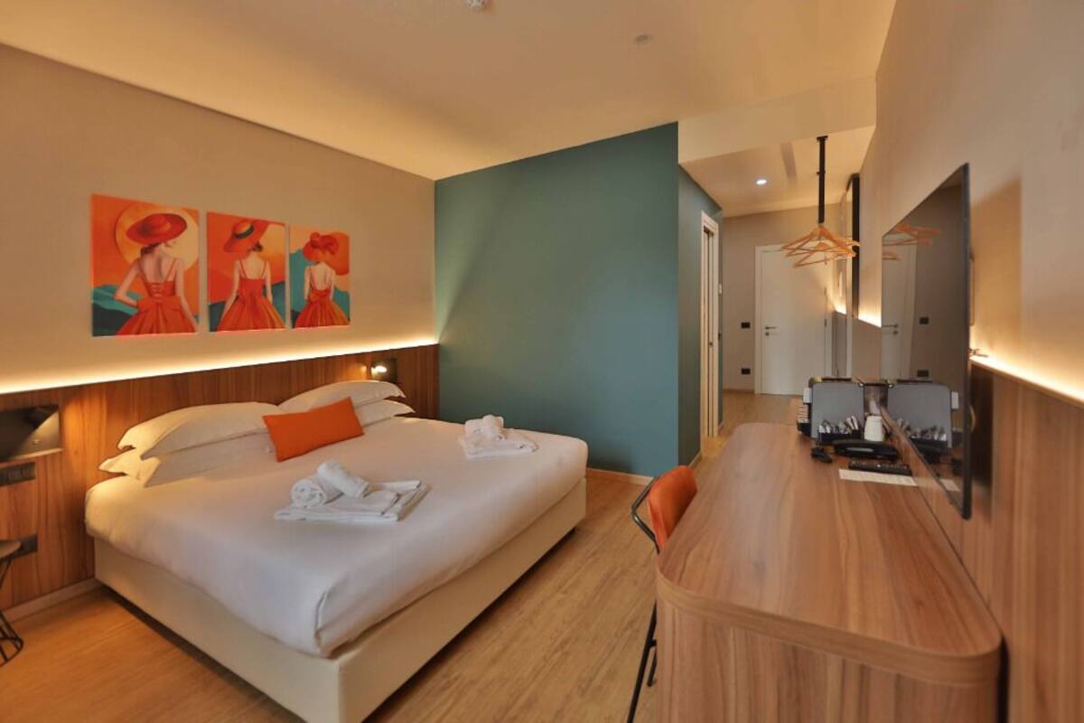 A modern hotel room with a large bed, a desk, and a mirror.