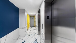 Un passadís modern amb sòl de marbre, una paret blava i un ascensor metàl·lic.