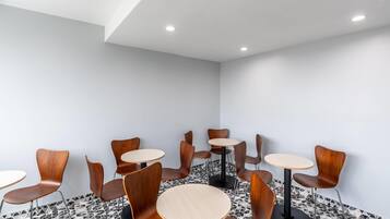 Un interior moderno con mesas redondas y sillas de madera, suelo de baldosas e iluminación empotrada en el techo.